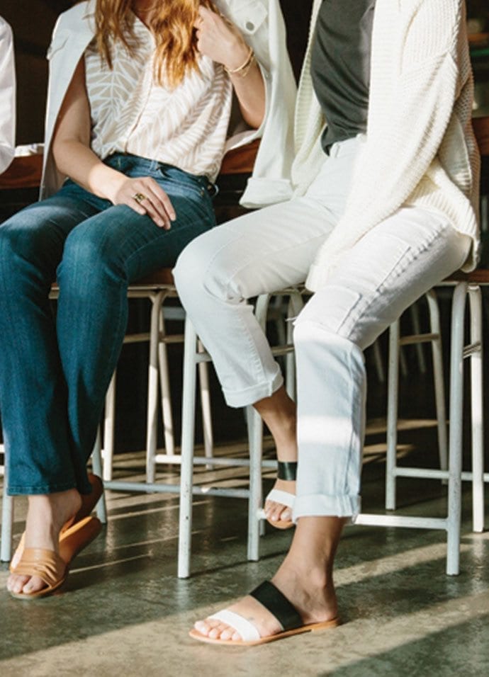 Two women seen from the neck down sitting on stools in casual summer wear